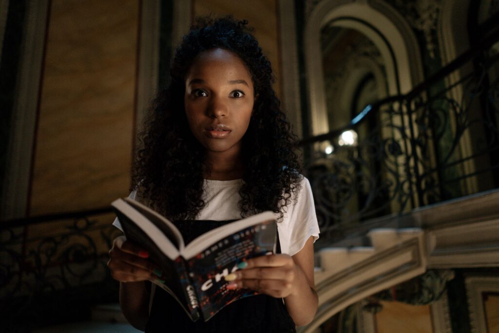 A Black girl looking shocked while holding a book.